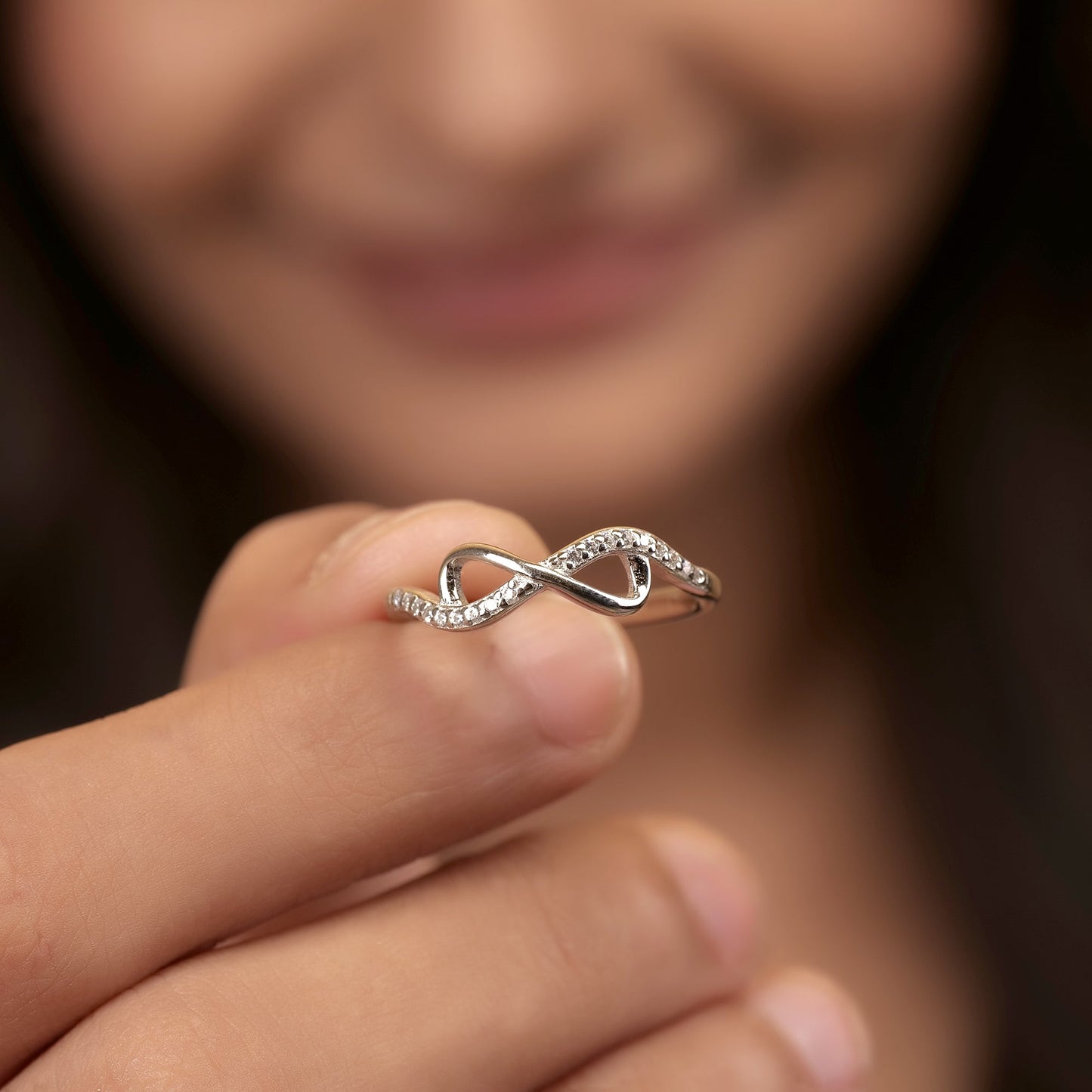 Silver infinity ring on a finger with a blurred background