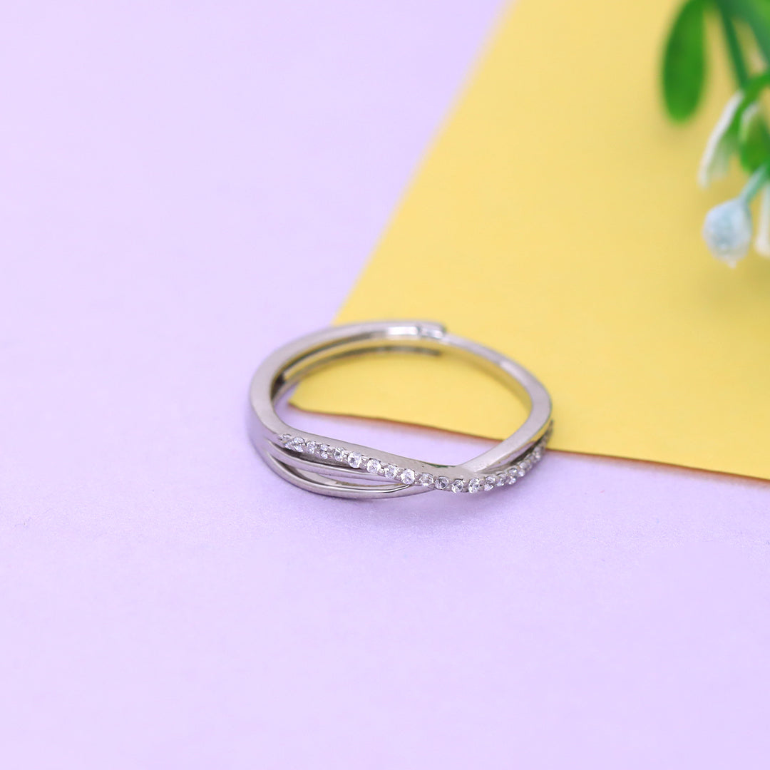 Silver ring with small diamonds on a purple surface with a yellow card and green plant in the background